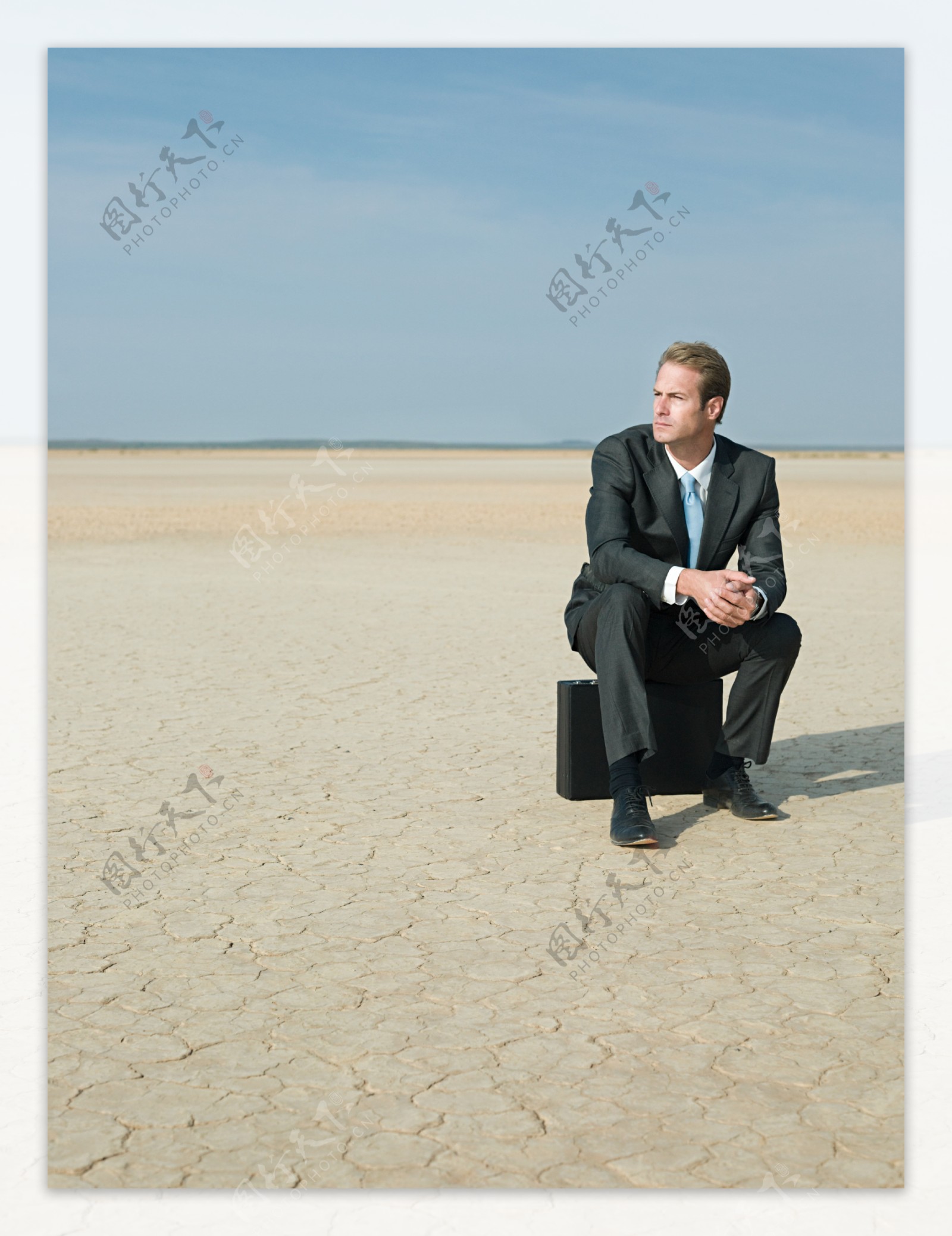 在沙漠中坐在皮箱上的商业男人图片