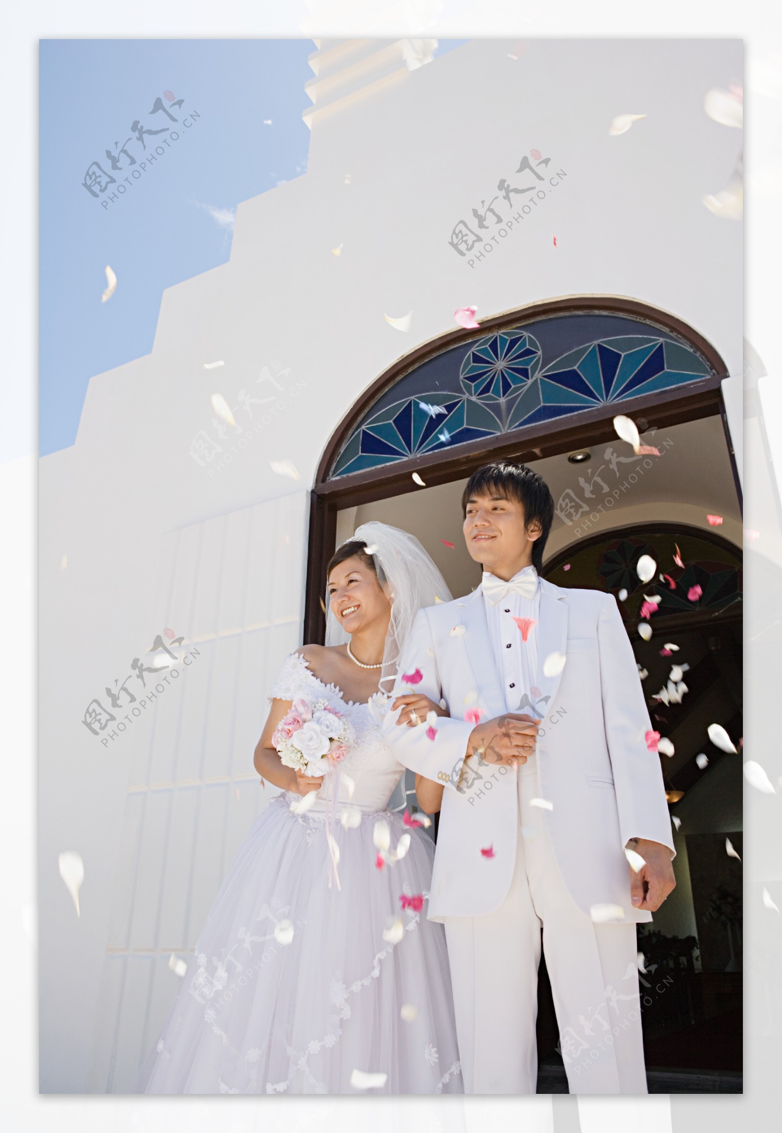礼堂前看着飘落花瓣微笑的新郎新娘图片图片
